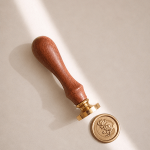 Siegelstempel mit goldenem Messingkopf und Holzgriff und goldenem Wachssiegel mit Rosenmotiv in einem minimalistischem Hintergrund