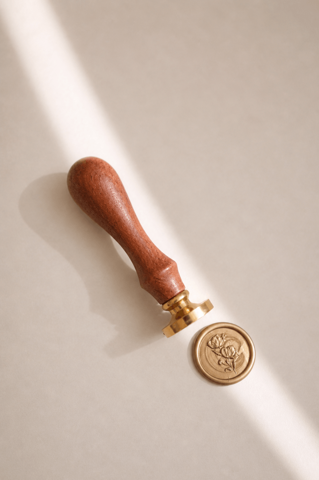 Siegelstempel mit goldenem Messingkopf und Holzgriff und goldenem Wachssiegel mit Rosenmotiv in einem minimalistischem Hintergrund