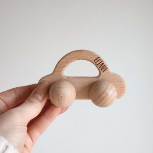 Auto aus Holz mit Rädern und Namensgravur "Eliana" von einer Hand gehalten vor einem neutralen Hintergrund