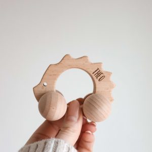 Igel aus Holz mit Rädern und Namensgravur "Theo" von einer Hand gehalten vor einem neutralen Hintergrund