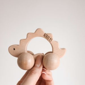 Dinosaurier aus Holz mit Rädern und Namensgravur "Nikolas" von einer Hand gehalten vor einem neutralen Hintergrund