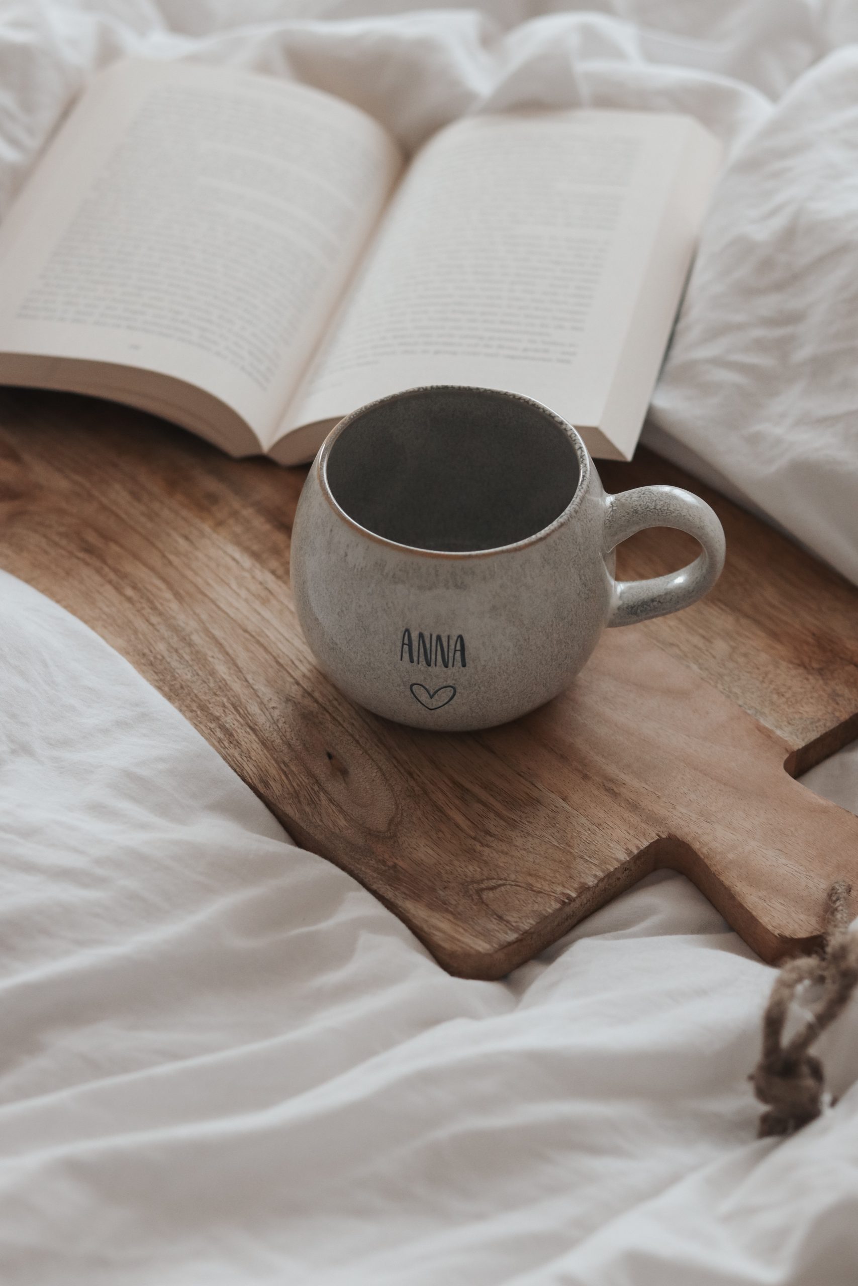 Tasse personalisiert. große beige graue Keramiktasse mit graviertem Wunschtext auf einer weißen Decke mit einem Schneidebrett aus Holz und einem aufgeschlagenen Buch im Hintergrund