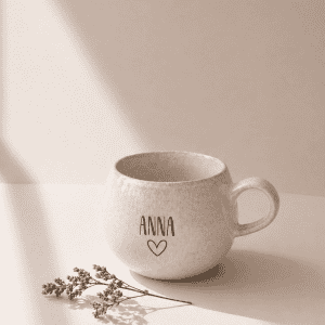 große beige Tasse mit Namensgravur "Anna" mit Herz in einem neutralen Hintergrund