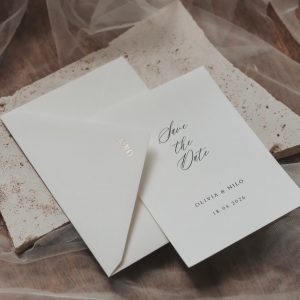 Weißer Briefumschlag mit einer Save the Date Karte mit goldenen Buchstaben auf der Lasche.