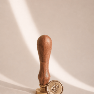 Siegelstempel mit goldenem Messingkopf und Holzgriff und goldenem Wachssiegel mit Rosenmotiv in einem minimalistischem Hintergrund