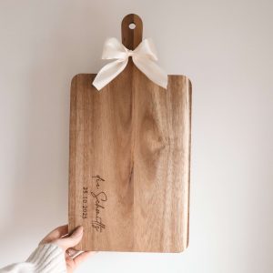 Holzbrett mit weißer Schleife am Griff und Namensgravur auf dem Brett