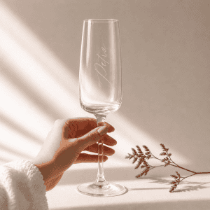 Sektglas mit Gravur "Petra" in einem minimalistischen Hintergrund mit natürlichem Sonnenlicht und zartem Zweig von einer Hand gehalten
