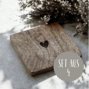 Das Bild zeigt einen Holzuntersetzer in quadratischer Form mit einem mittig platzierten kleinen Herz als Gravur. Auf einem Steinboden mit natürlichem Sonnenlicht und dekorativen Trockenblumen