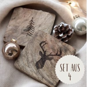 Das Bild zeigt zwei Holzuntersetzer in quadratischer Form mit einem mittig platzierten Tanne und Rentier als Gravur. Auf einem Steinboden mit dekorativen Tannenzweigen, Glaskugeln und Tannenzapfen