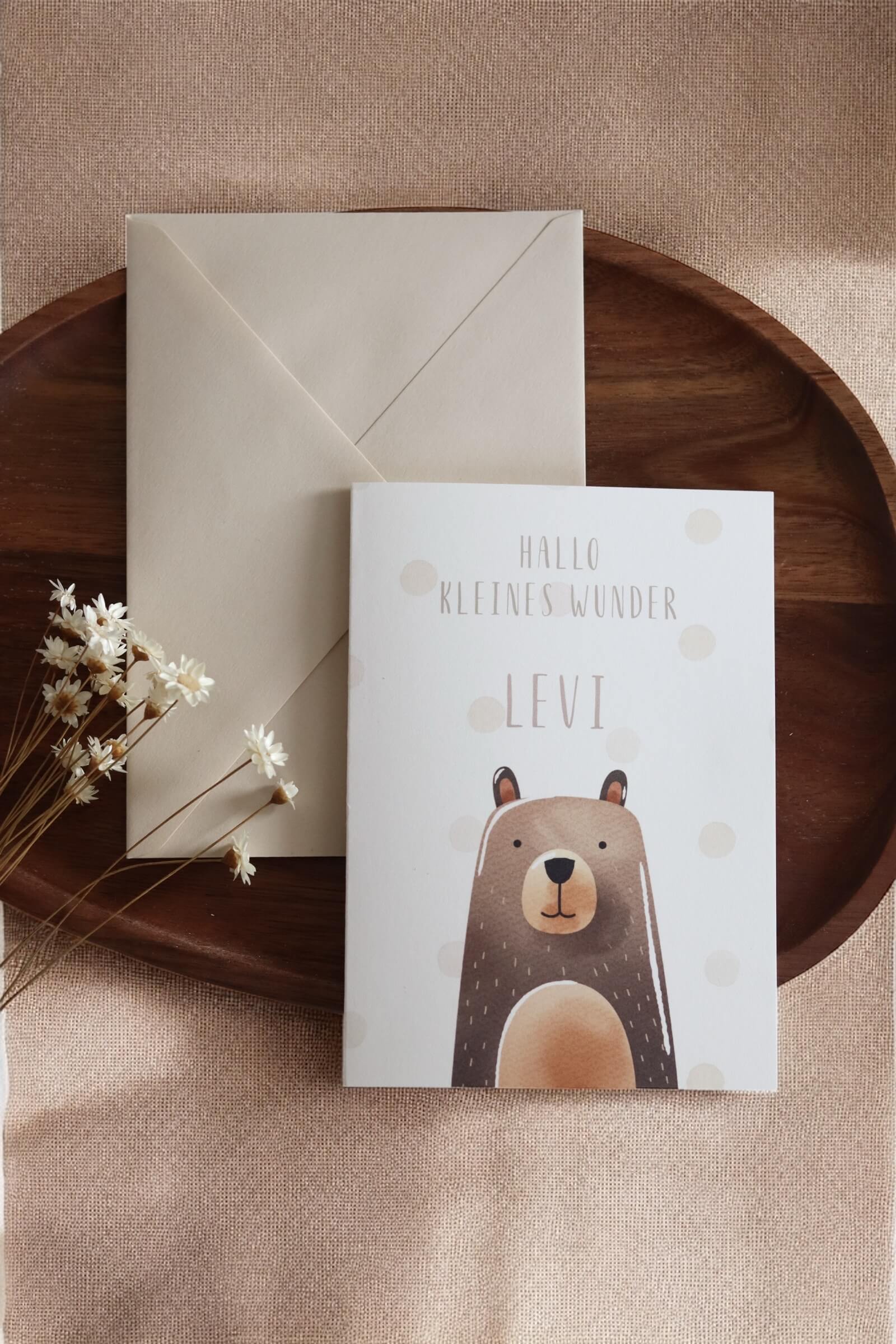 Grußkarte im Postkarten format mit Bärenmotiv und Namen daneben einer beiger Umschlag auf einem Holztablett und Trockenblumen