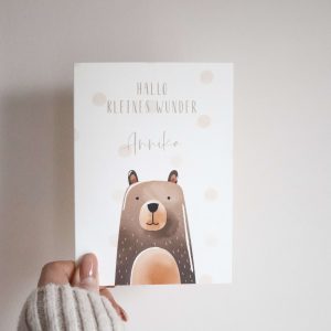 weiße Karte im Postkartenformat mit Bärenmotiv und dem Text "Hallo kleines Wunder Annika" von einer Hand gehalten vor einem neutralen Hintergrund