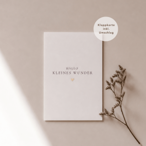 Eine weiße Grußkarte liegt mittig und zeigt den Schriftzug "Hallo kleines Wunder“ mit einem goldenen Herz darunter. Rechts neben der Karte liegt ein feiner, getrockneter Zweig, während weiches Licht und sanfte Schatten für eine ruhige, natürliche Atmosphäre sorgen.