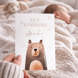 Glückwunschkarte "Hallo kleines Wunder Annika" mit Bärenaquarell und Punkten, im Hintergrund ein schlafendes baby