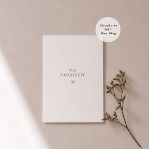 Eine weiße Grußkarte liegt mittig und zeigt den Schriftzug "zur Hochzeit“ mit einem goldenen Herz darunter. Rechts neben der Karte liegt ein feiner, getrockneter Zweig, während weiches Licht und sanfte Schatten für eine ruhige, natürliche Atmosphäre sorgen.