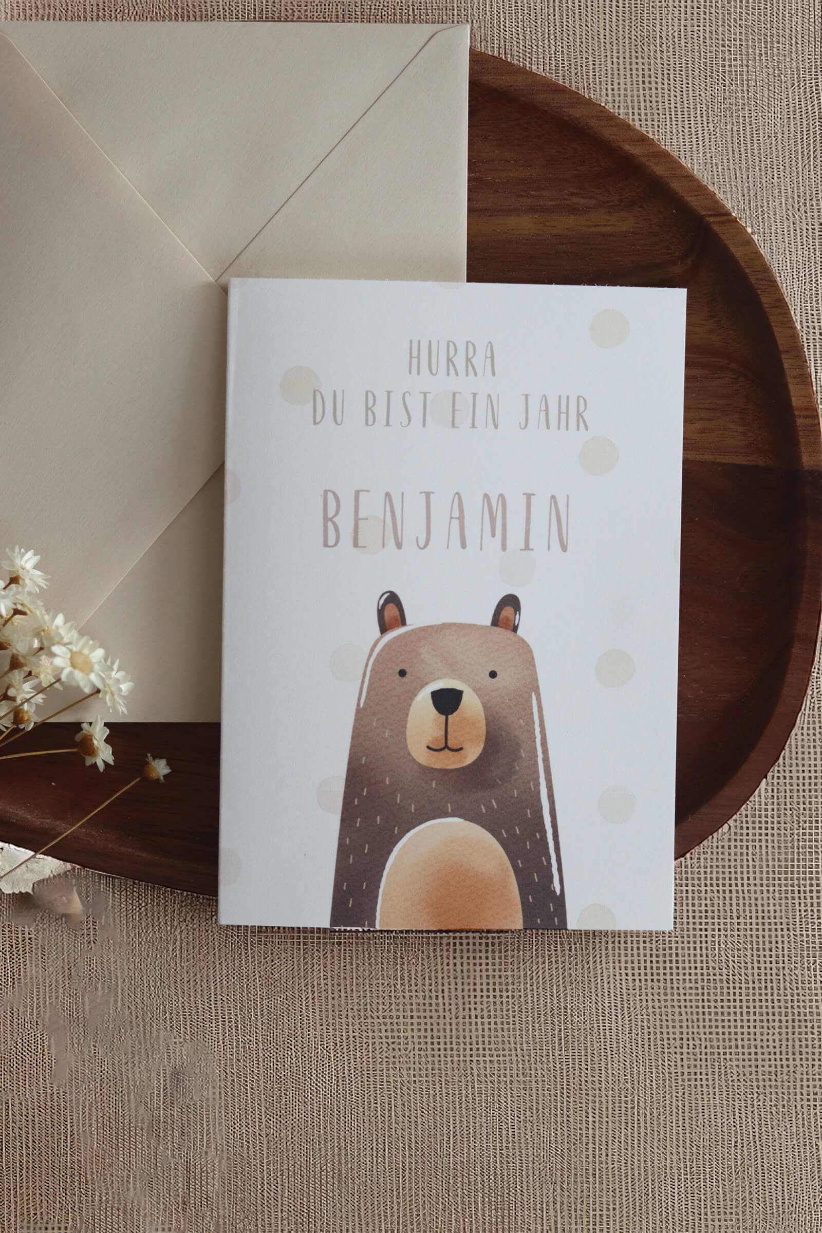 Grußkarte im Postkarten format mit Bärenmotiv und Namen daneben einer beiger Umschlag auf einem Holztablett und Trockenblumen