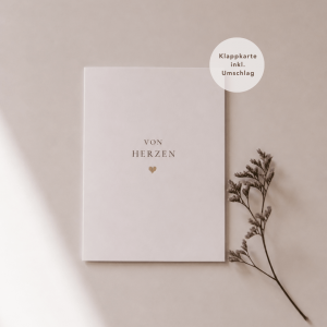Eine weiße Grußkarte liegt mittig und zeigt den Schriftzug "von Herzen“ mit einem goldenen Herz darunter. Rechts neben der Karte liegt ein feiner, getrockneter Zweig, während weiches Licht und sanfte Schatten für eine ruhige, natürliche Atmosphäre sorgen.