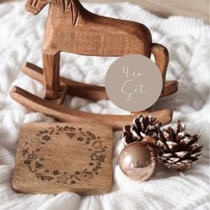 Quadratischer Untersetzer aus Mangoholz graviertem Weihnachtsmotiv auf einem hellen Stoffuntergrund und weihnachtlicher Dekoobjekte