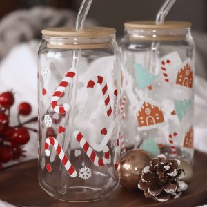 zwei große Trinkgläser mit weihnachtlichem Motiv mit Zuckerstangen und Lebkuchenhäusern mit Bambusdeckel und Glasstrohhalm.