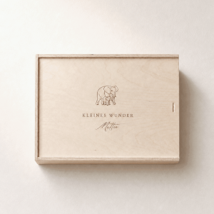 Personalisierte Erinnerungsbox aus hellem Holz mit eingraviertem Elefantenmotiv und Namen auf einem minimalistischen, cremefarbenen Hintergrund mit weichem Tageslicht.