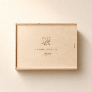 Personalisierte Erinnerungsbox aus hellem Holz mit eingraviertem Elefantenmotiv und Namen auf einem minimalistischen, cremefarbenen Hintergrund mit weichem Tageslicht.