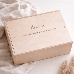 Erinnerungskiste aus hellem Buchenholz mit Schiebedeckel und gravierten Namen und Geburtsdaten auf einer hellen Decke