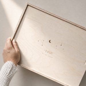 Minimalistische Aufnahme einer hellen Holzbox mit Gravur ‚Valentin‘ und Sternen-Motiv auf einem hellen Greige-Hintergrund mit einem sanften Sonnenstrahl.