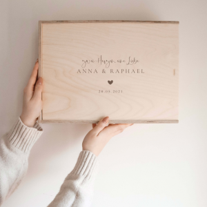 Personalisierte Erinnerungskiste aus Naturholz mit Gravur „Zwei Herzen.Eine Liebe“ und Datum, schlichtes Design, wird vor hellem Hintergrund in der Hand gehalten.