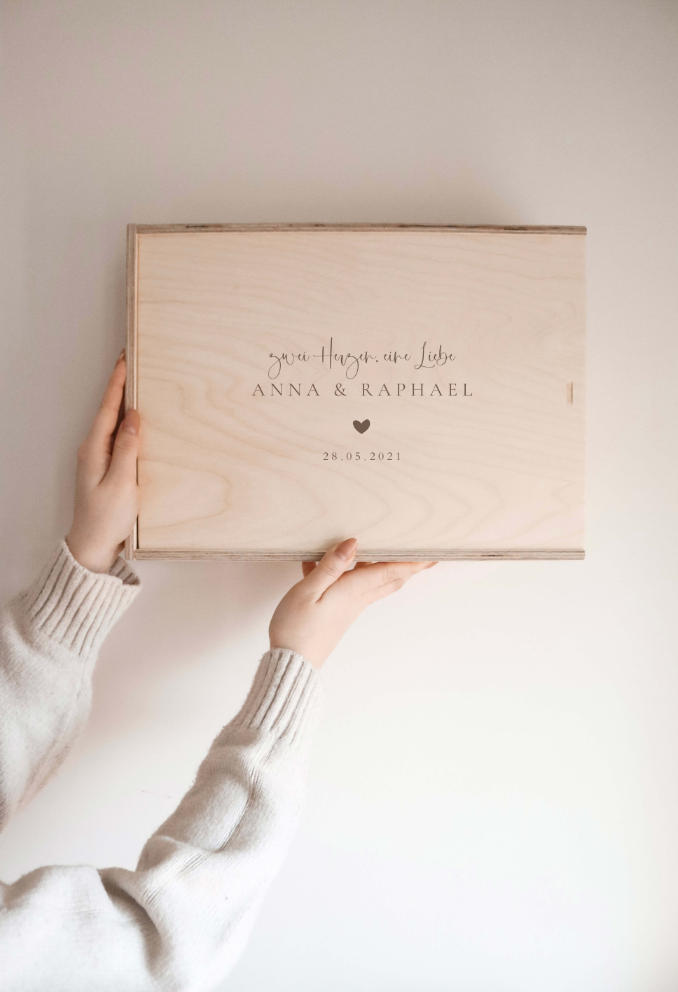 Personalisierte Erinnerungskiste aus Naturholz mit Gravur „Zwei Herzen.Eine Liebe“ und Datum, schlichtes Design, wird vor hellem Hintergrund in der Hand gehalten.