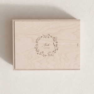 Personalisierte Erinnerungsbox aus hellem Holz mit eingraviertem Motiv mit Waldtieren und Namen auf einem minimalistischen, cremefarbenen Hintergrund mit weichem Tageslicht.