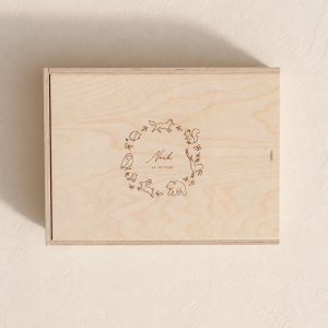 Personalisierte Erinnerungsbox aus hellem Holz mit eingraviertem Waldtiermotiv und Namen auf einem minimalistischen, cremefarbenen Hintergrund mit weichem Tageslicht.