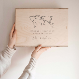 Personalisierte Erinnerungskiste aus Naturholz mit Gravur „Unserer schönsten Reiseerinnerungen", schlichtes Design, wird vor hellem Hintergrund in der Hand gehalten.