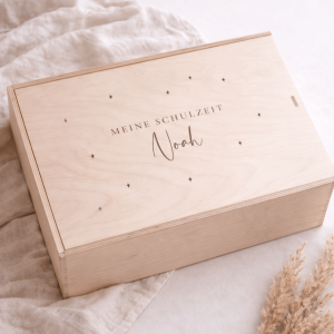 Erinnerungskiste aus hellem Buchenholz mit Schiebedeckel und gravierten Namen und Text "Meine Schulzeit" auf einer hellen Decke