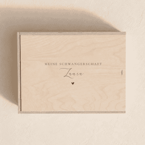 Personalisierte Erinnerungsbox aus hellem Holz mit eingraviertem Text "Meine Schwangerschaft" und einem Herz auf einem minimalistischen, cremefarbenen Hintergrund mit weichem Tageslicht.