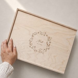Minimalistische Aufnahme einer hellen Holzbox mit Gravur ‚Noah‘ und Waldtier-Motiv auf einem hellen Greige-Hintergrund mit einem sanften Sonnenstrahl.