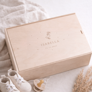Erinnerungskiste aus hellem Buchenholz mit Schiebedeckel und gravierten Namen und Gansmotiv auf einer hellen Decke und Babyschuhen und einem Schnuller