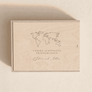 Personalisierte Erinnerungsbox aus hellem Holz mit eingravierter Weltkarte und Spruch "Unsere schönsten Erinnerungen" minimalistischen, cremefarbenen Hintergrund mit weichem Tageslicht.