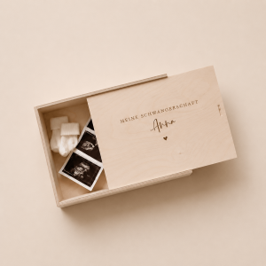 Minimalistische Aufnahme einer personalisierten Holz-Erinnerungskiste mit Gravur „meine schwangerschaft Anna" mit Mutterpass, Babysocken und Ultraschallbildern und einem Herz, auf hellem Hintergrund mit sanftem Sonnenlicht.