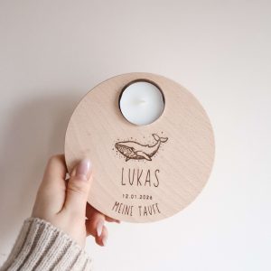 Runder Holzteller aus hellem Buchenholz mit dem Motiv eines Wals und dem Text "Lukas, meine Taufe", von einer Hand gehalten vor einem neutralen Hintergrund