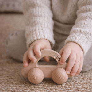 Kleinkind mit personalisiertem Greifling aus Holz in Form eines Autos