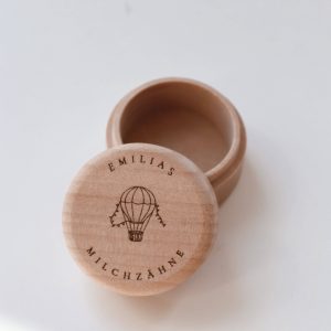 Helle runde Holzdose mit dem eingravierten Text "Emilias Milchzähne" und einem Ballonmotiv in minimalistischem Hintergrund