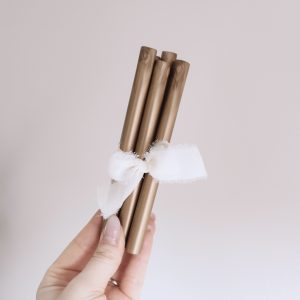 Siegelwachsstangen in gold bronze mit einer weißen Schleife von einer Hand gehalten vor einem neutralen Hintergrund