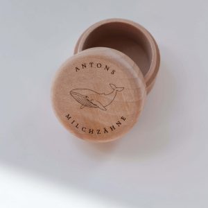 Helle runde Holzdose mit dem eingravierten Text "Antons Milchzähne" und einem Walmotiv in minimalistischem Hintergrund