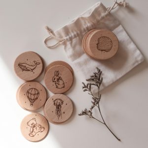 Memoryspiel aus runden Holzscheiben mit kindgerechten Motiven und einem Jutebeutel aus weißem Stoff vor einem neutralen Hintergrund