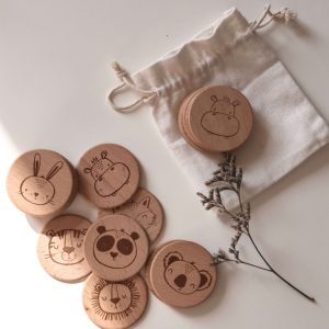 Memoryspiel aus runden Holzscheiben mit kindgerechten Motiven und einem Jutebeutel aus weißem Stoff vor einem neutralen Hintergrund