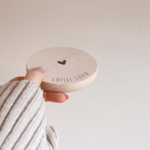 helle runde Holzscheibe mit dem Text "Coffee Lover" und einem Herz in der Mitte von einer Hand gehalten vor einem neutralen Hintergrund