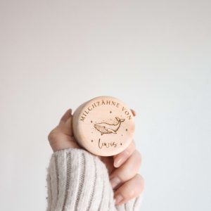 Runde helle Holzdose mit einem Namen und einem Wal Motiv von einer Hand haltend vor neutralem Hintergrund
