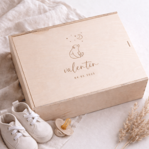 Erinnerungskiste aus hellem Buchenholz mit Schiebedeckel und gravierten Namen und Bärmotiv auf einer hellen Decke und Babyschuhen und einem Schnuller