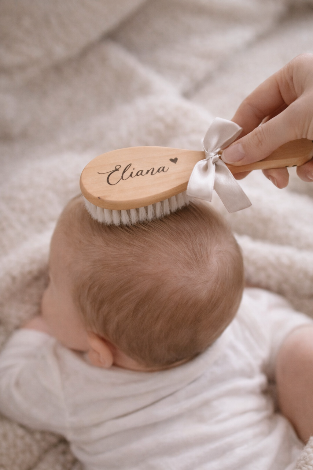 Baby auf dem Bauch liegend wird mit einer Babyhaarbürste mit Namen personalisiert über den Kopf gestrichen