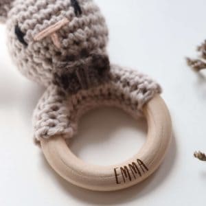 Gehäkelte Babyrassel in Form eines Hasen an einem Holzring mit Namensgravur in einem neutralen Setting