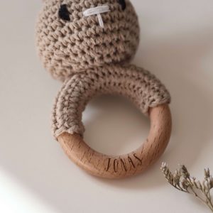 Gehäkelte Babyrassel in Form eines Hasen an einem Holzring mit Namensgravur in einem neutralen Setting